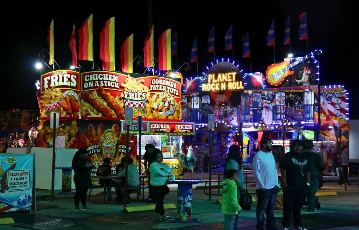People walk around food vendors and a fun house at a fair.