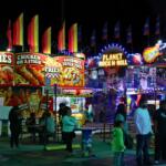People walk around food vendors and a fun house at a fair.