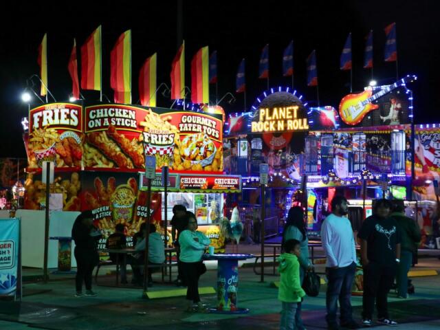 People walk around food vendors and a fun house at a fair.