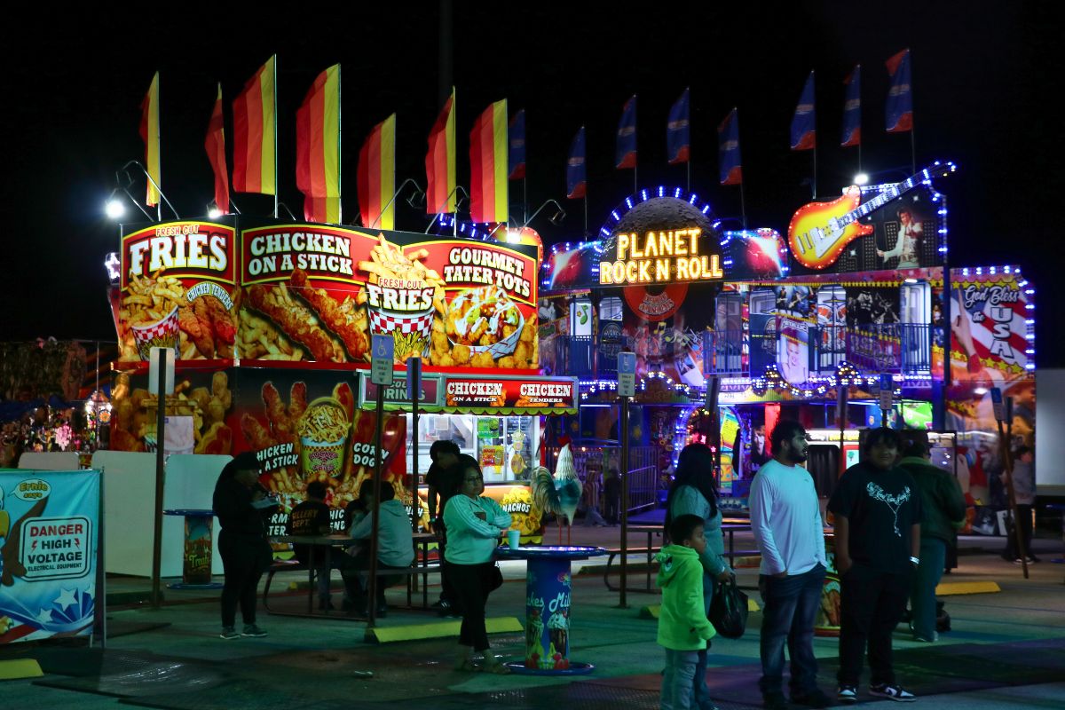 People walk around food vendors and a fun house at a fair.