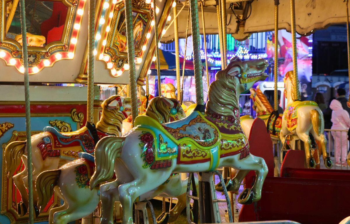 A merry-go-round is dimly lit on one side a brightly lit on the other. It spins with no guests on it.