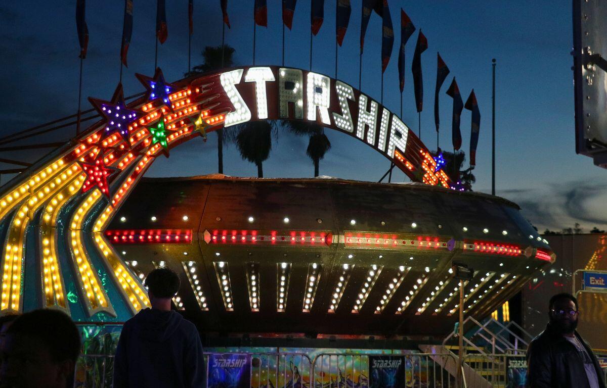 A large, metal, spinning ride features a large sign above it reading, "Starship." Guests stand around it as it spins.
