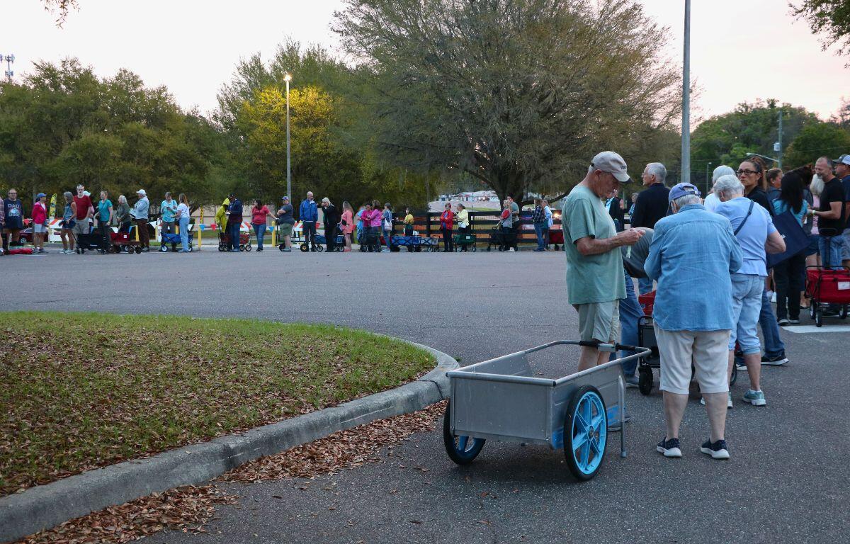 A line of people with wagons circles in a parking lot, waiting to enter an event.