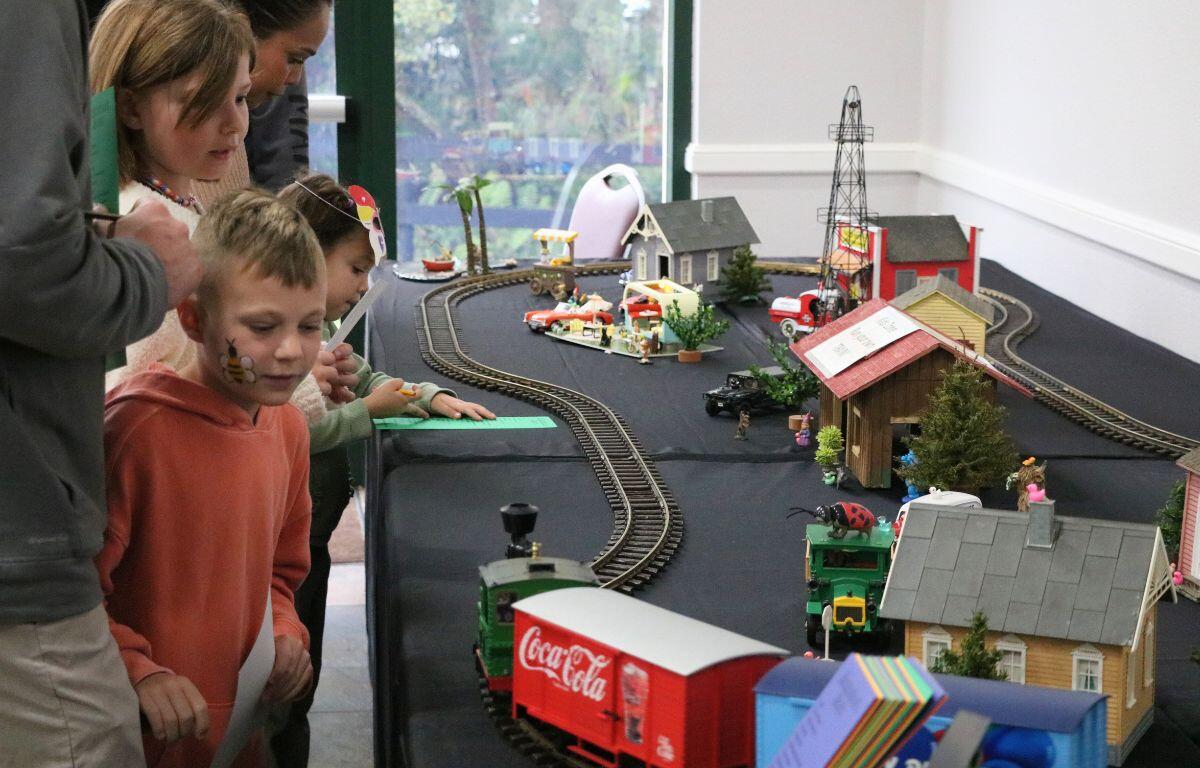 A toy train display sits on a table with a black tablecloth as children watch it go around the track.