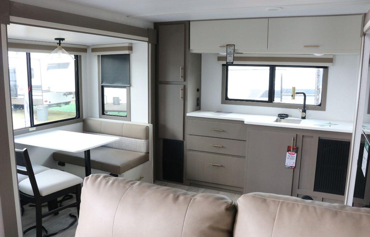 The interior of an RV features a small dining area, a long kitchen toward the back and a sofa in the middle of the room. Windows around the room brighten the interior.