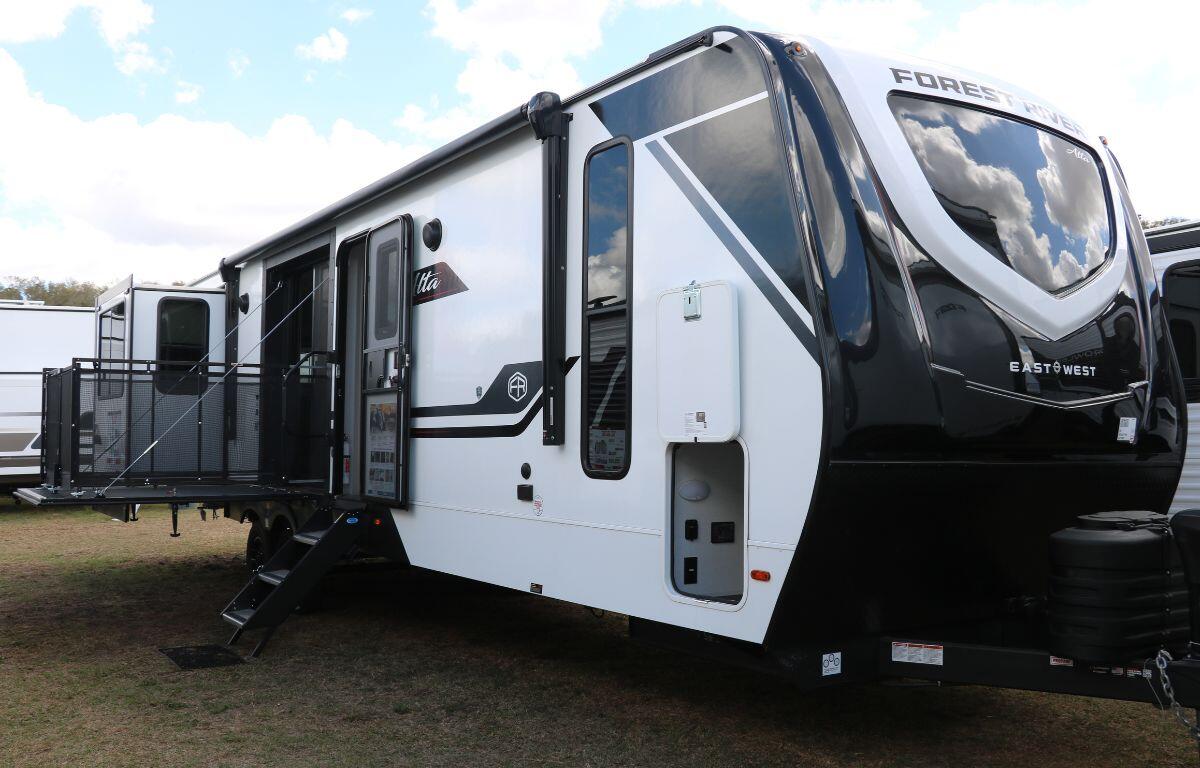 A large RV stands in a grass field. The RV features a special section with a retractable balcony. More RVs surround it.