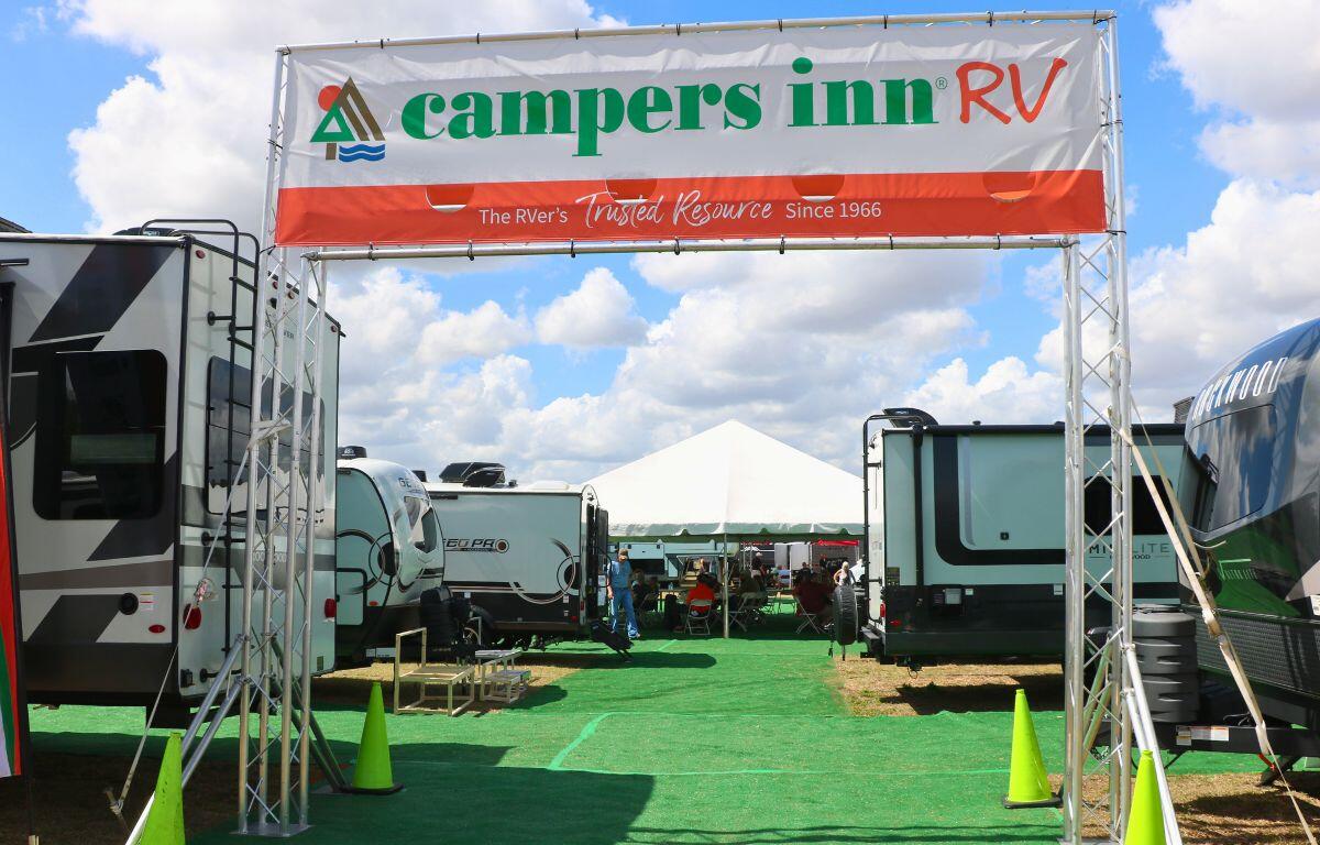 Campers Inn RV features a tall, entryway with a banner with the name displayed on it and RVs in the background.
