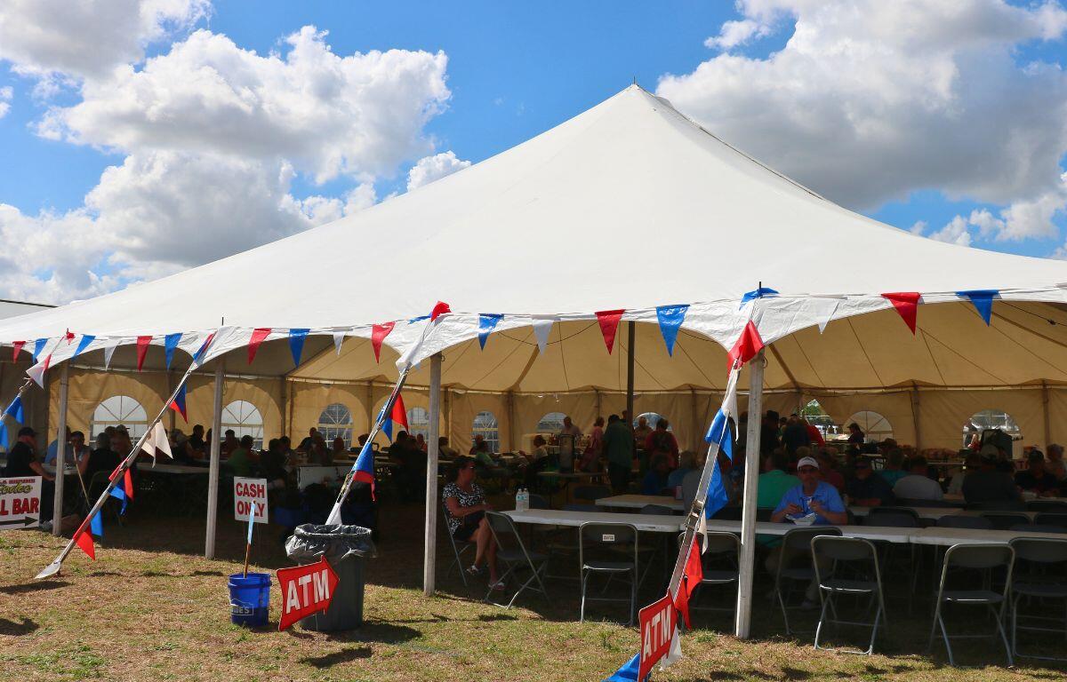 A large, white canopy features multiple white tables with red, white and blue decorative flags on it. Toward the back are concession stands.