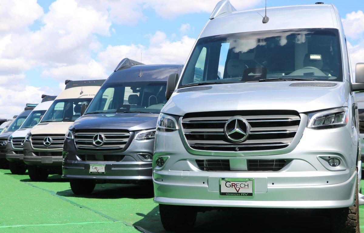Mercedes-Benz motorhomes are lined up on green flooring in a large field.