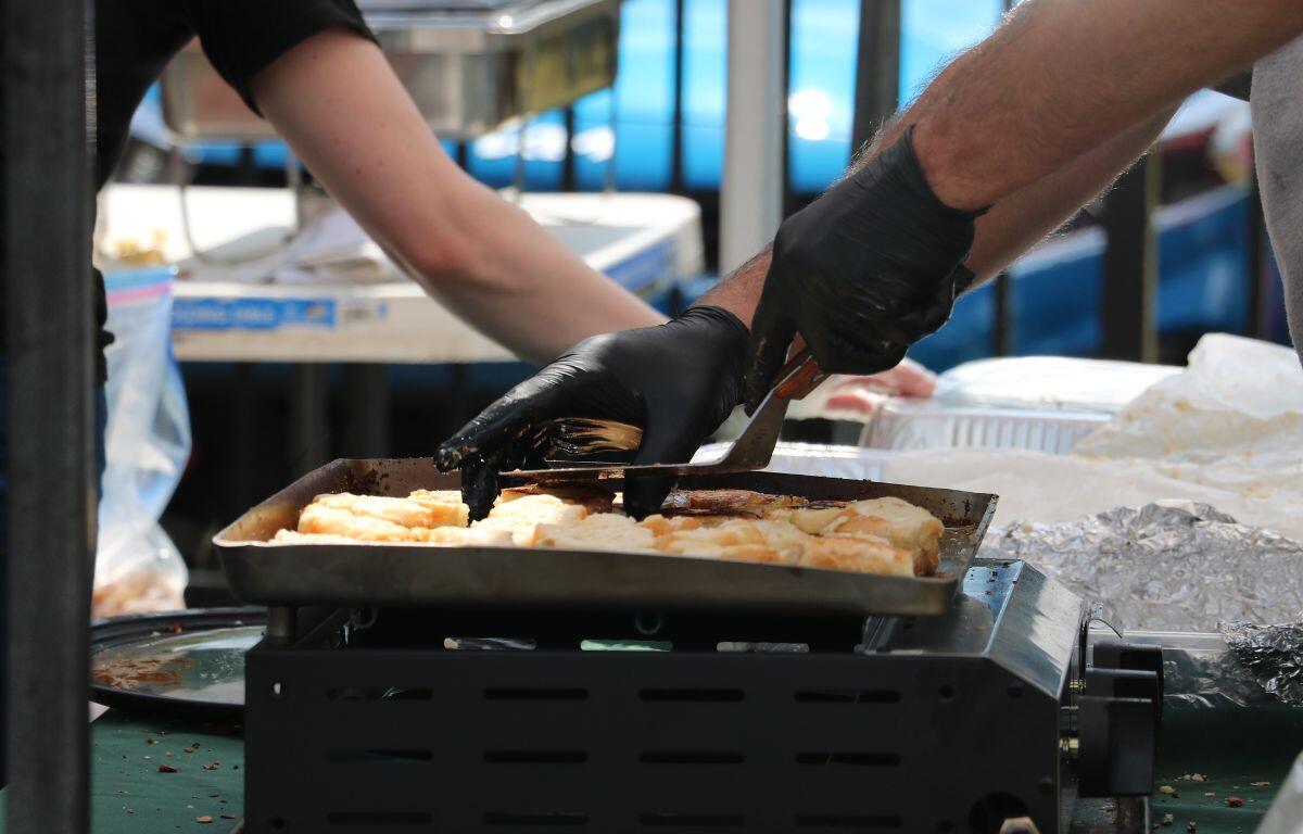 A man makes grilled cheese on a small burner while a person behind him prepared a carrier for the food.