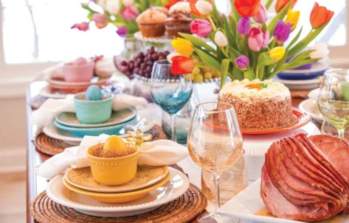 A colorful table display with tulips, roasted ham and colored cups and plates.