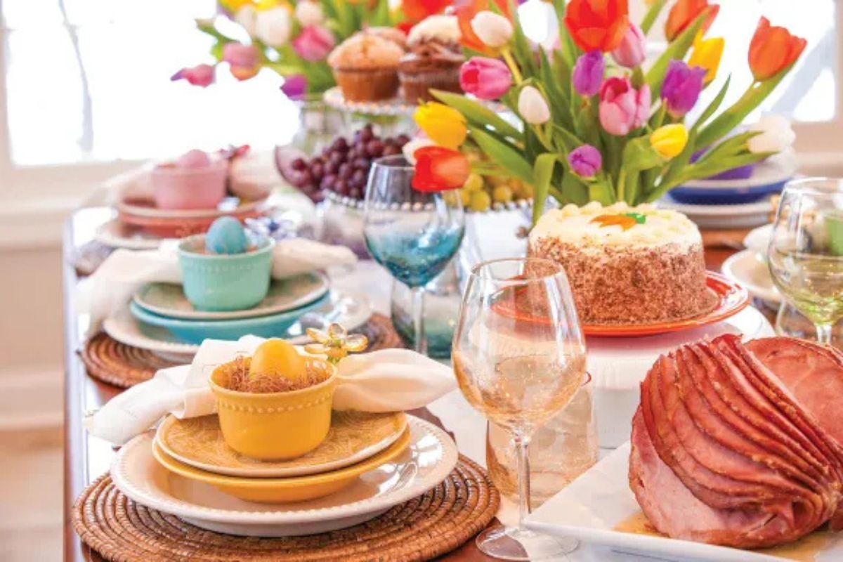A colorful table display with tulips, roasted ham and colored cups and plates.