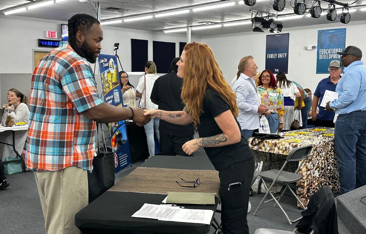 A job seeker shakes hands with a recruiter across a table at a hiring event.