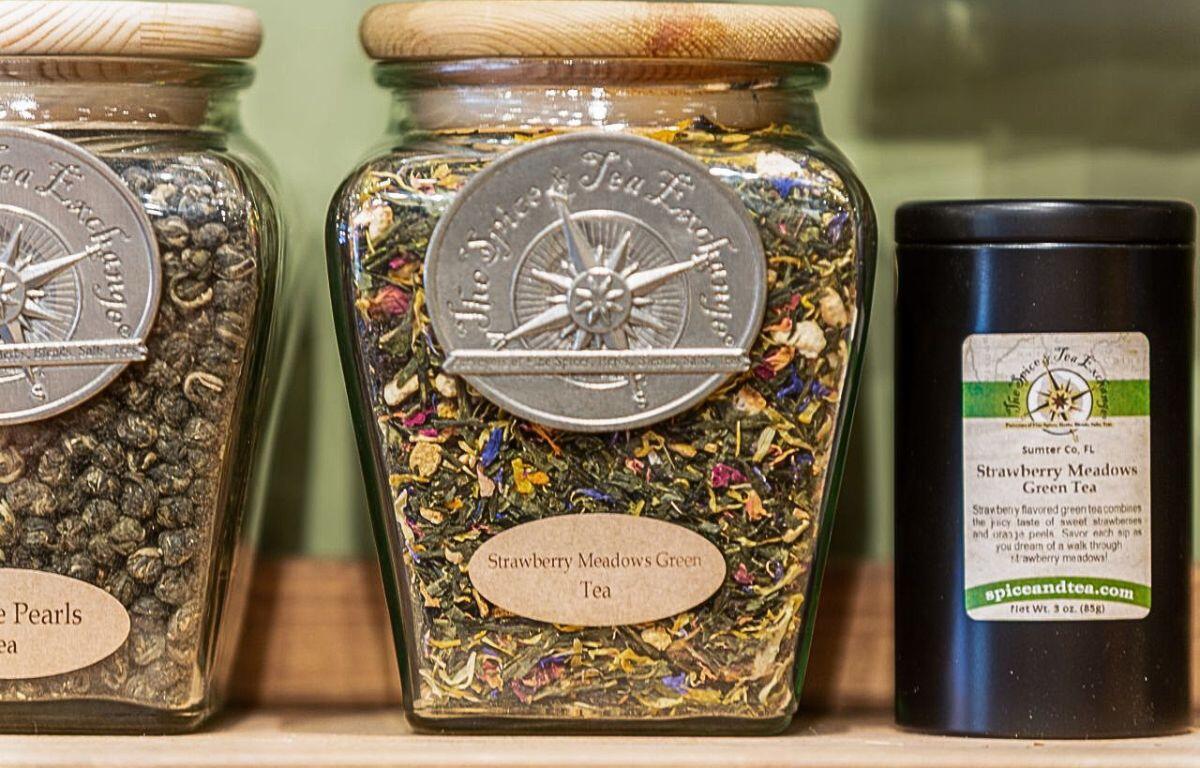 A closeup of glass jars of tea leaves sitting on a wooden shelf.