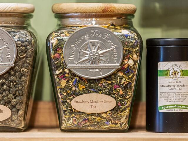 A closeup of glass jars of tea leaves sitting on a wooden shelf.