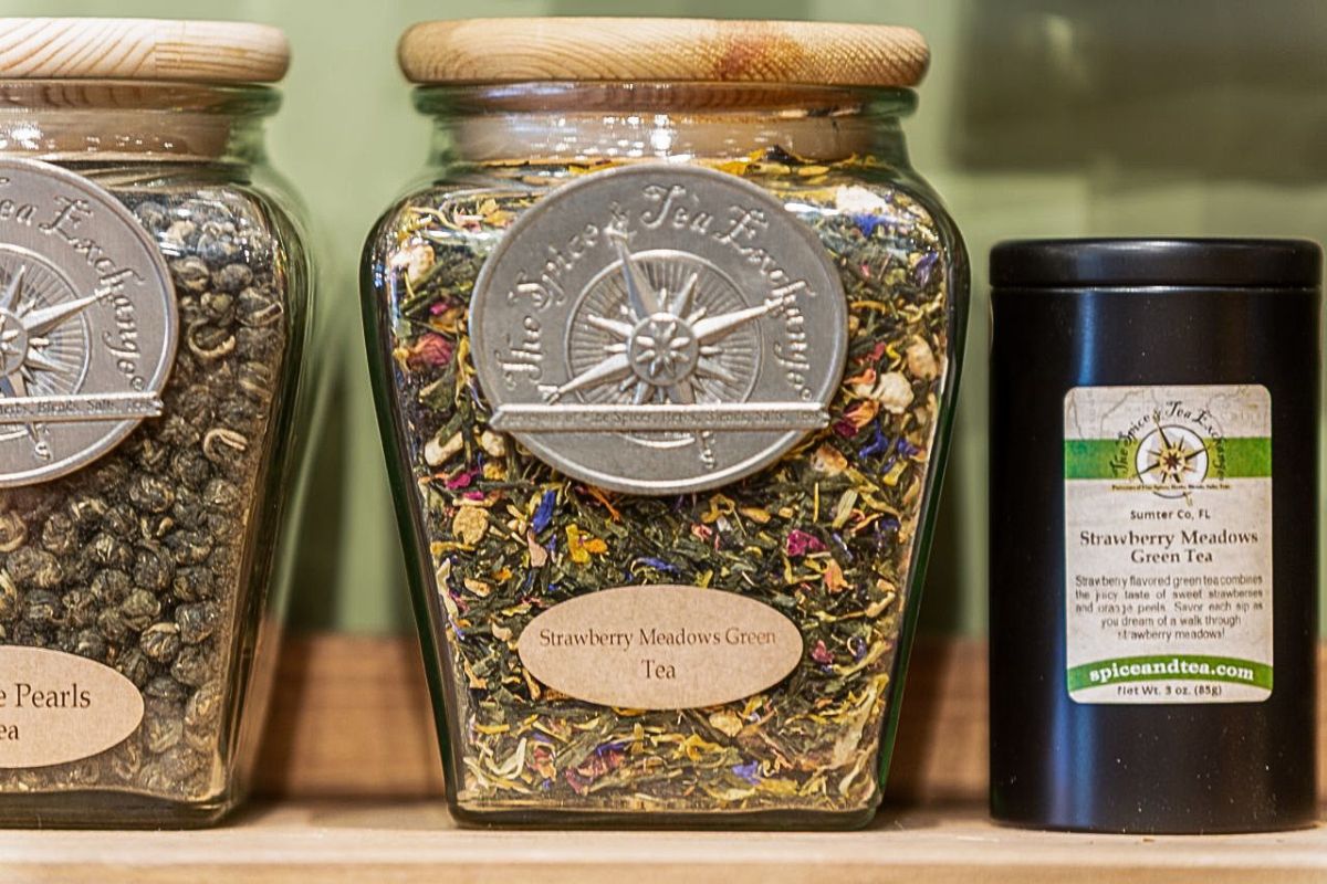 A closeup of glass jars of tea leaves sitting on a wooden shelf.