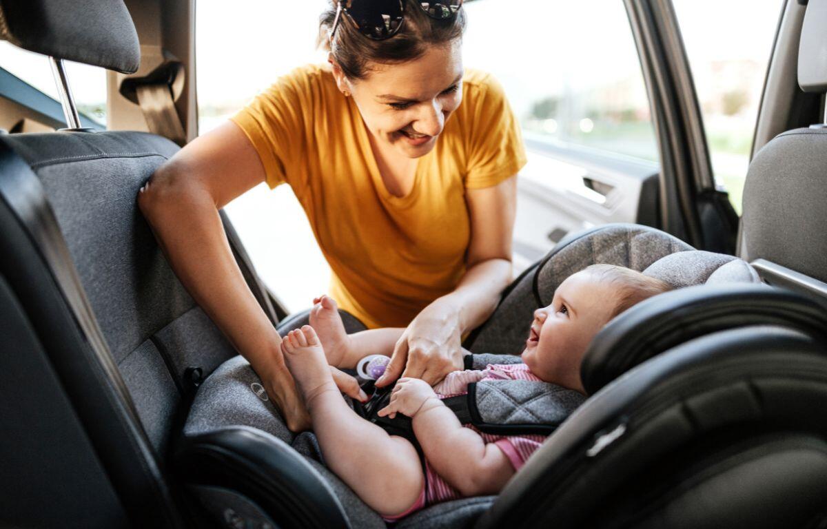 Colored image of a women in an orange shirt strapping a children into a car seat.