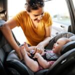 Colored image of a women in an orange shirt strapping a children into a car seat.