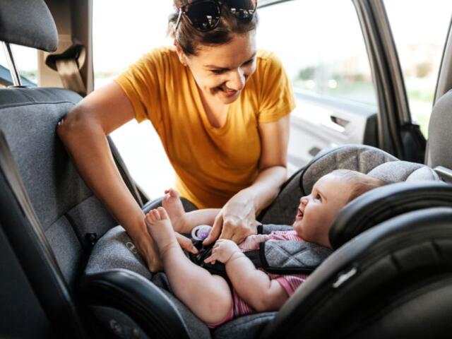 Colored image of a women in an orange shirt strapping a children into a car seat.