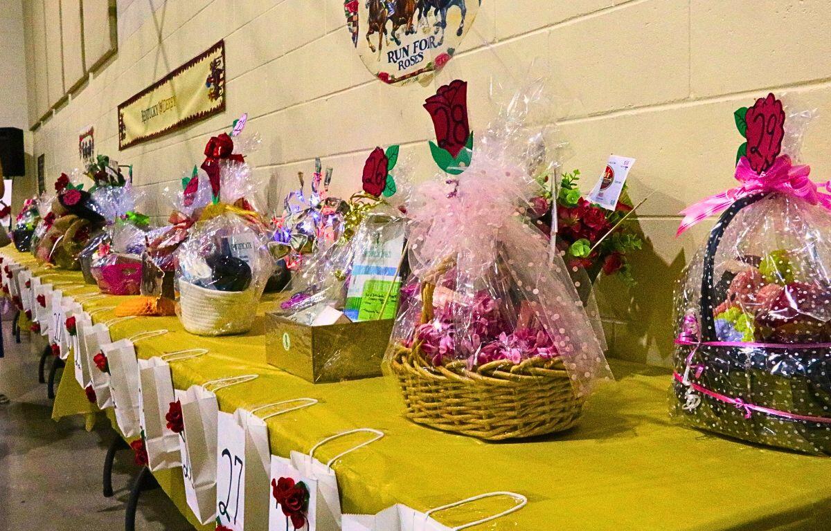 Rows of wrapped gift baskets and prize baskets on a long yellow table at a fundraiser, each with numbered tags.