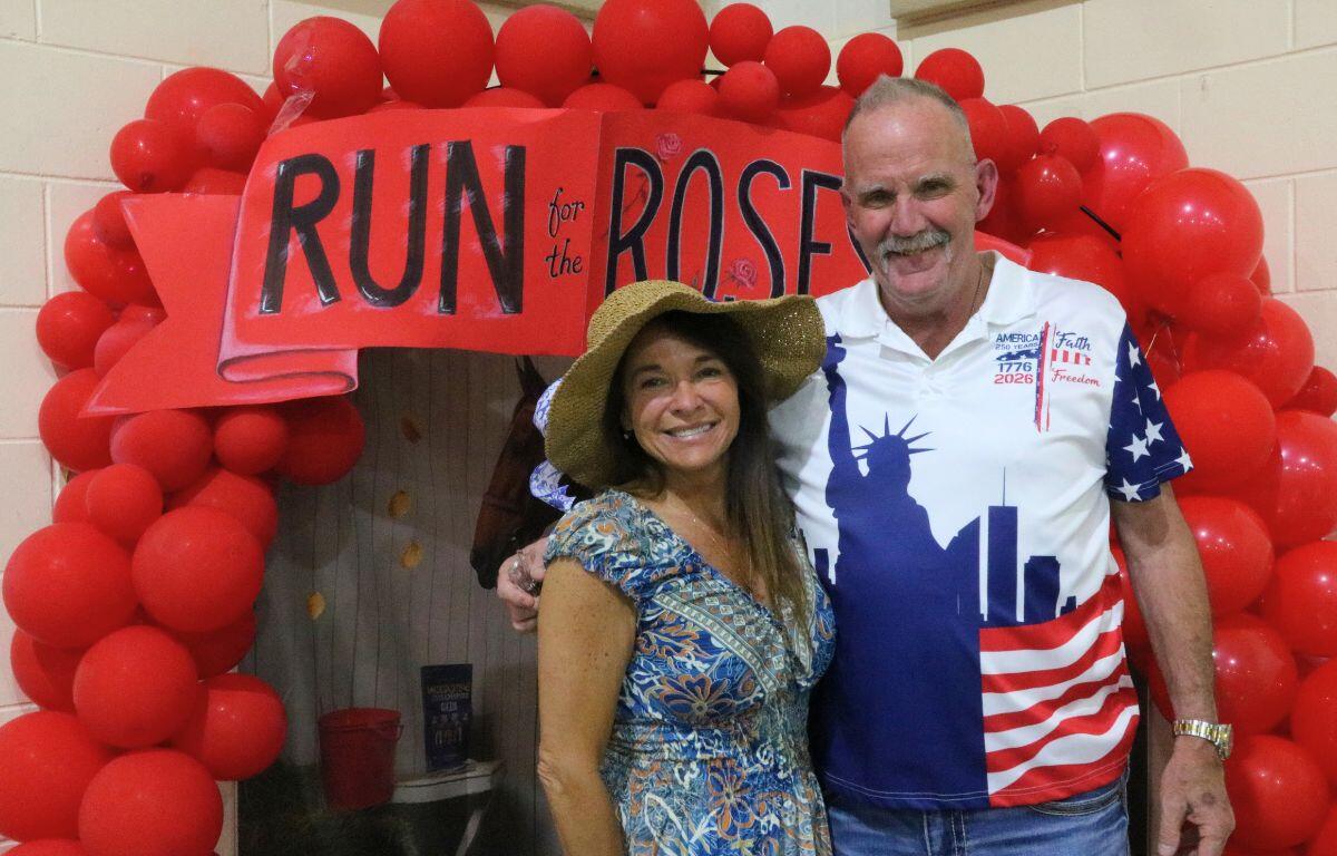 Two people posing under a red balloon arch with a banner that reads 'RUN for the ROSE' at a charity event.