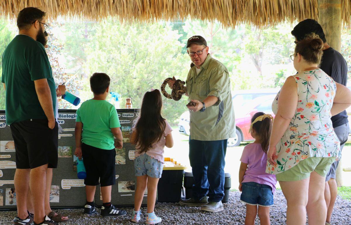 A man demonstrates a tortoise and snake to children and families under a chickee.
