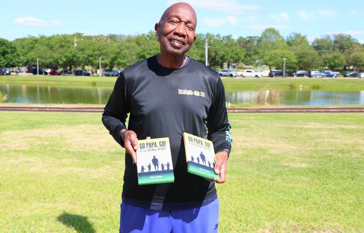 A man holds two copies of his books in his hands while standing in front of a lake. The books are titled Go Papa Go.