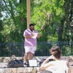 A man stands on a stage with a piece of paper, reading his poetry to an audience of people.