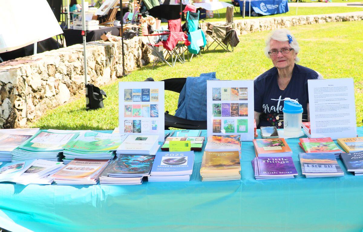 A woman sits behind a table with multiple books scattered around.