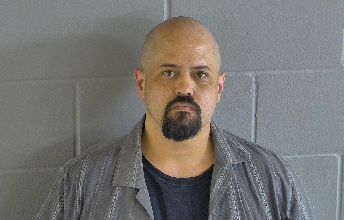 A colored image of a bald man with a goatee posed in front of a grey wall.