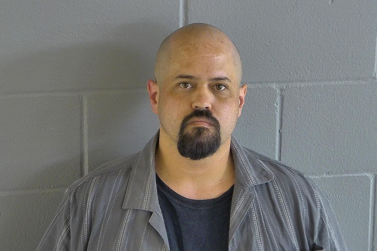 A colored image of a bald man with a goatee posed in front of a grey wall.