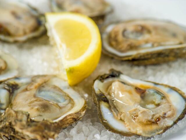 Five oysters laying on crushed ice, with a lemon garnished in the center.