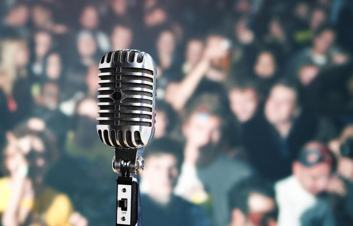 A colored image of a blurry crowd with a picture of a microphone in the foreground.