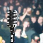 A colored image of a blurry crowd with a picture of a microphone in the foreground.