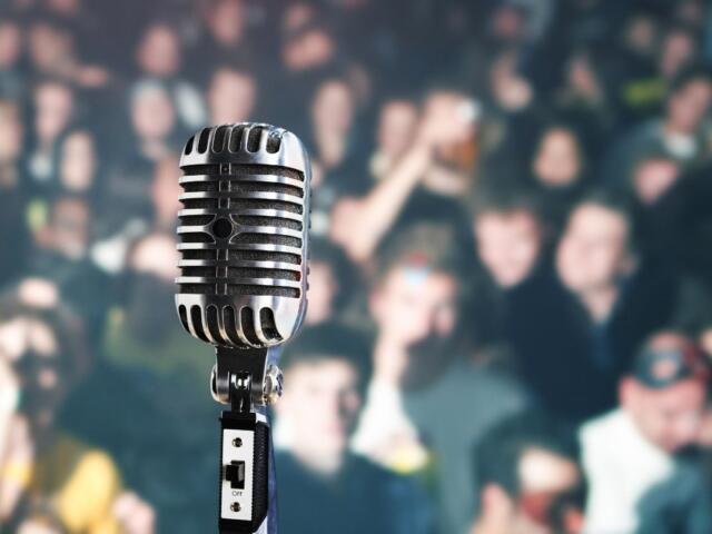 A colored image of a blurry crowd with a picture of a microphone in the foreground.