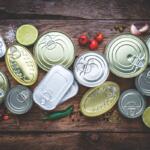 A colored image of canned goods top-down against a wooden background.