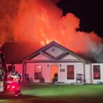A colored photo of a home on fire, with a firetruck in front.