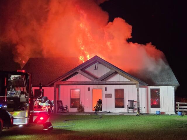A colored photo of a home on fire, with a firetruck in front.