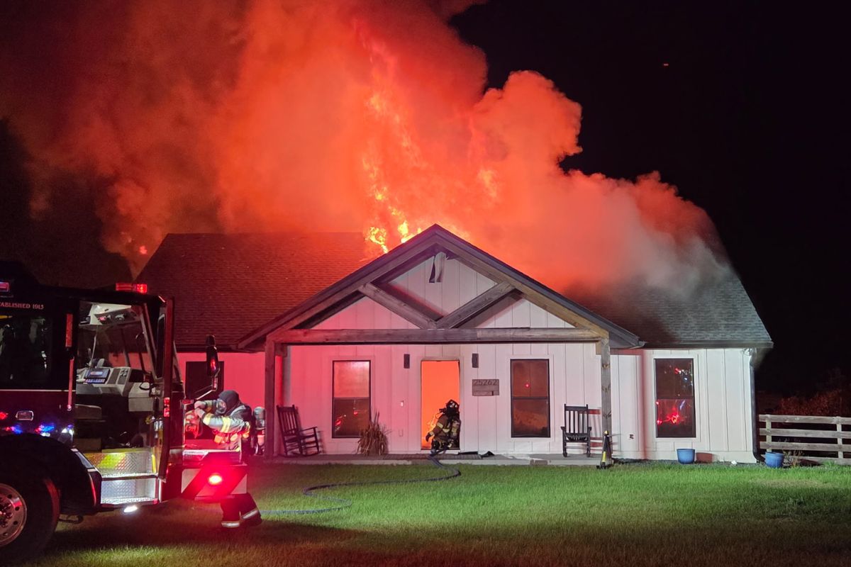 A colored photo of a home on fire, with a firetruck in front.