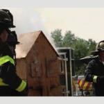 Two Sumter County firefighters putting on a demonstration by a miniature wooden house.