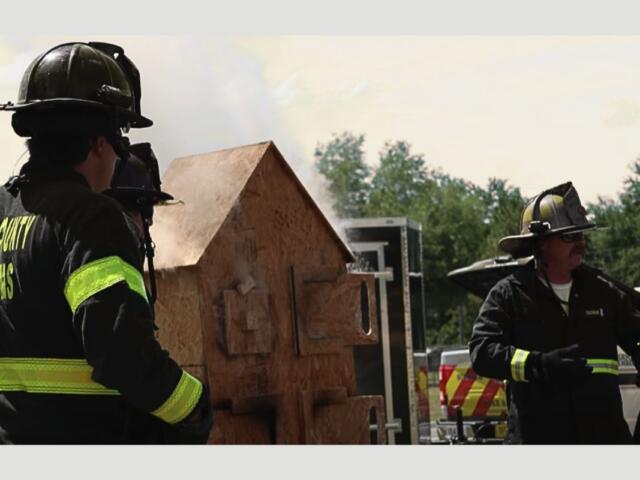 Two Sumter County firefighters putting on a demonstration by a miniature wooden house.