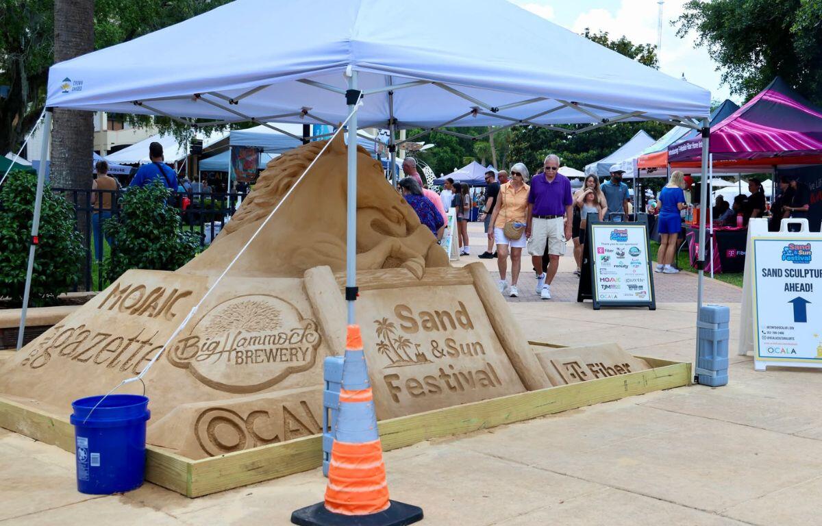 A sand sculpture advertising the Sand and Sun Festival underneath a white tent.