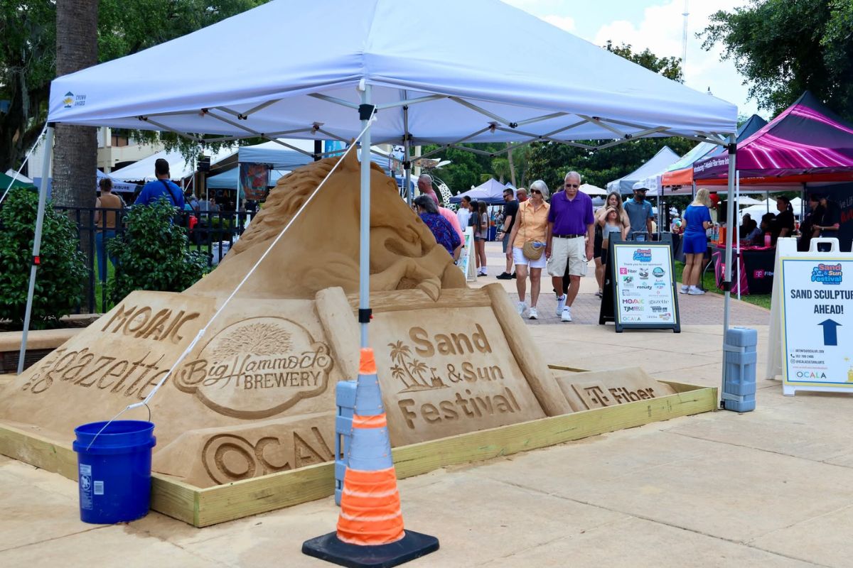 A sand sculpture advertising the Sand and Sun Festival underneath a white tent.