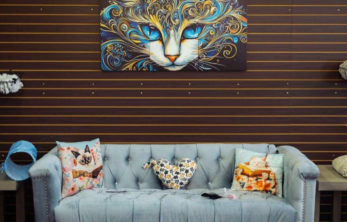 A cat painting hanging above a light blue couch with cat pillows.