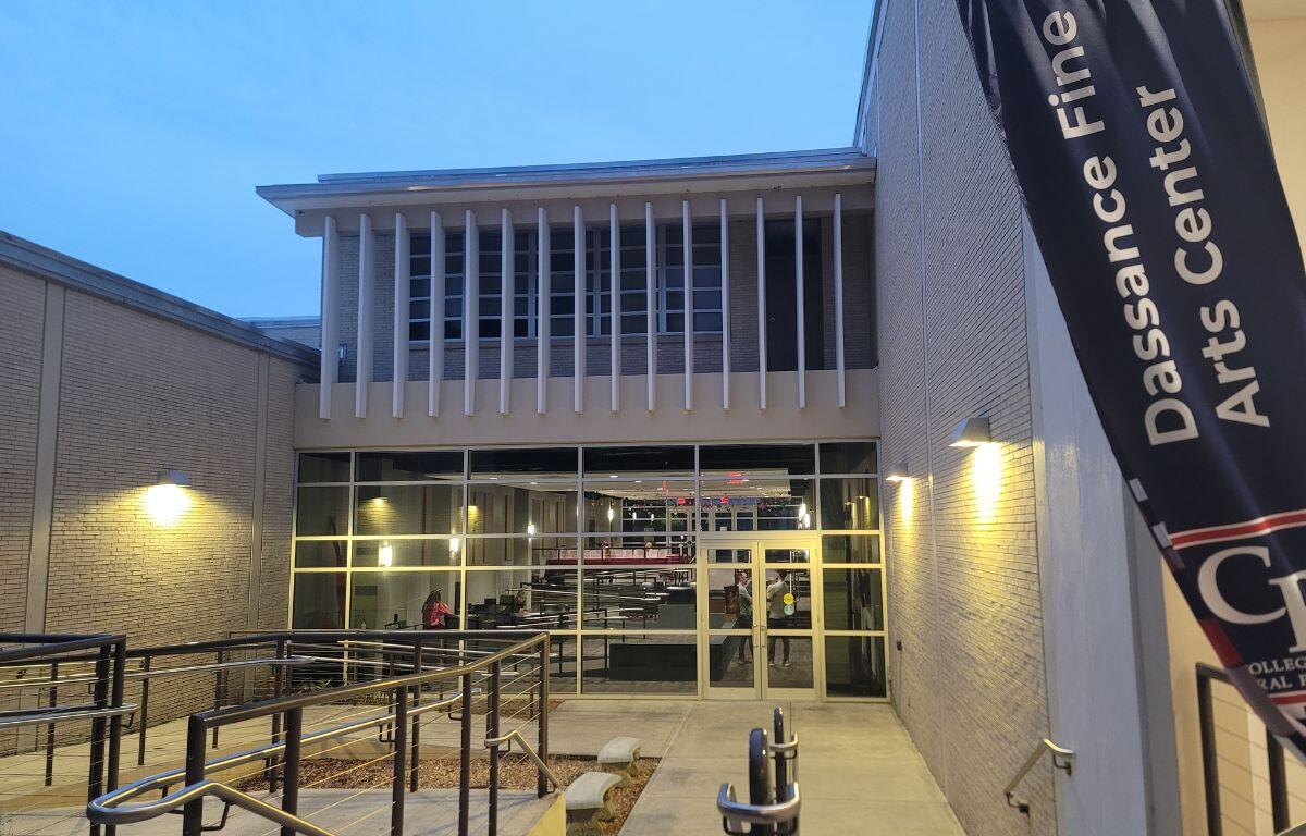 The exterior of a lobby outside of a theatre. A flag next to stair leading down into the lobby reads, "Dassance Fine Arts Center."