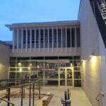 The exterior of a lobby outside of a theatre. A flag next to stair leading down into the lobby reads, "Dassance Fine Arts Center."