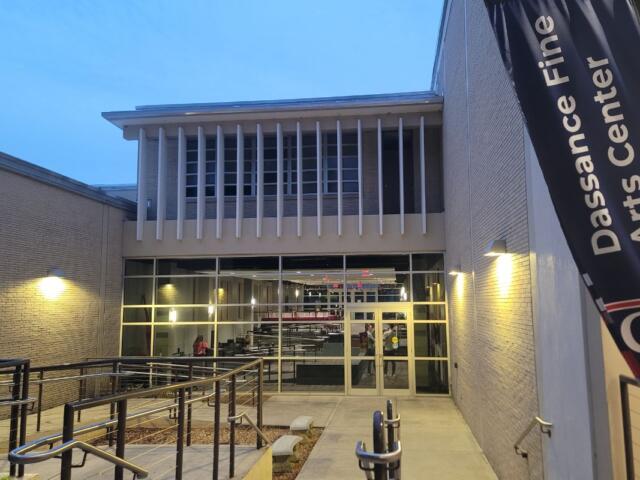 The exterior of a lobby outside of a theatre. A flag next to stair leading down into the lobby reads, "Dassance Fine Arts Center."