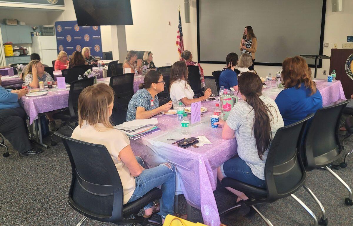 A group of women sit in a conference room, listening to a speaker.