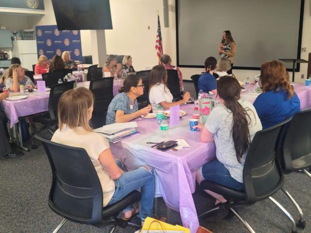 A group of women sit in a conference room, listening to a speaker.