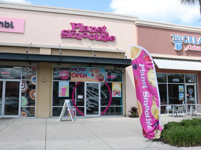 Exterior view of a shopping plaza. Three restaurants stand next to eachother, Crumbl, Planet Smoothie and The Great Mediterranean.